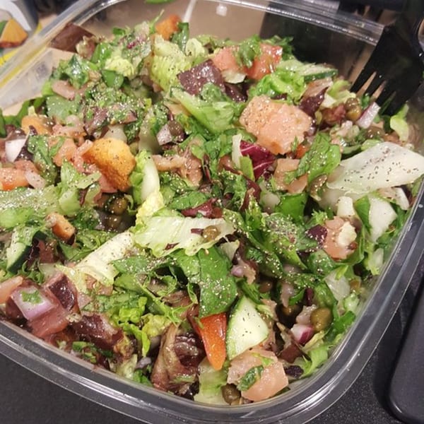 A Fourleaf Chopped Salad in a clear plastic container, filled with greens, salmon, and other toppings.