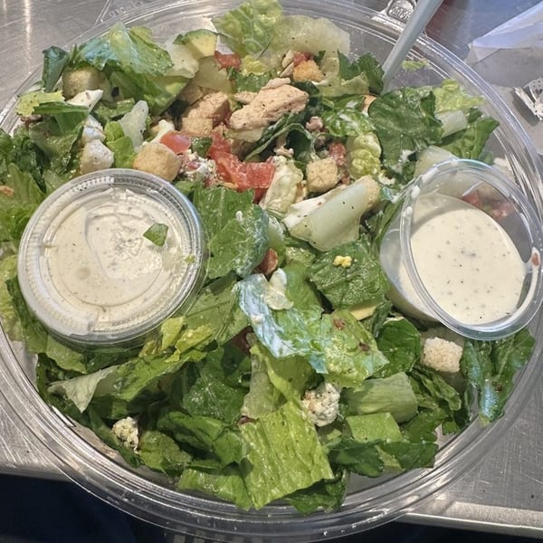 A Fourleaf Chopped Salad with lettuce, chicken, tomatoes, croutons, and two containers of dressing.