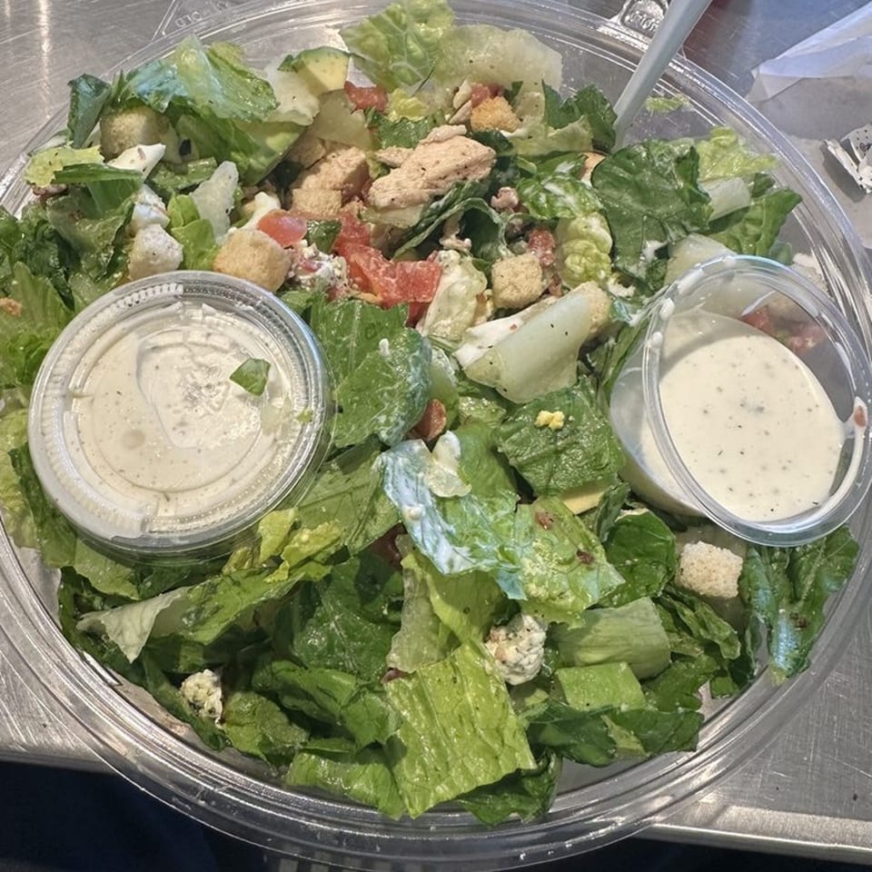 A Fourleaf Chopped Salad with lettuce, chicken, tomatoes, croutons, and two containers of dressing.